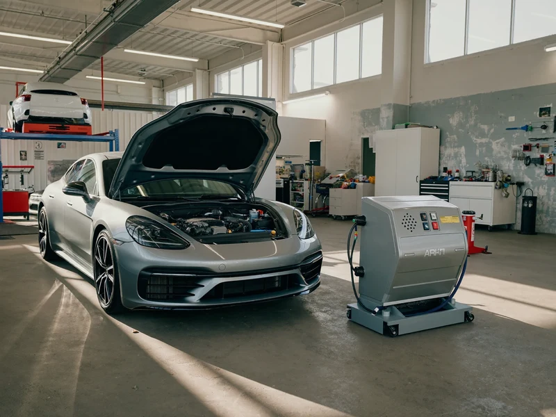 Illustrierte Werkstatthalle mit Pkw, geöffneter Motorhaube und Klimaservicegerät